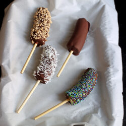 array of frozen chocolate bananas on a parchment lined tray.