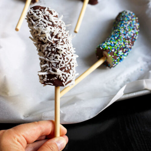 hand holding coconut and chocolate covered frozen banana on a stick.