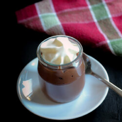 glass pot of chocolate pudding topped with whipped cream on white sauce with spoon.
