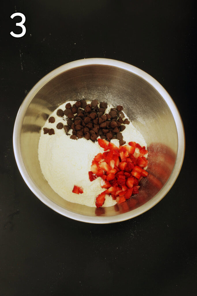 crumb mixture transferred to a metal mixing bowl with chocolate chips and chopped strawberries