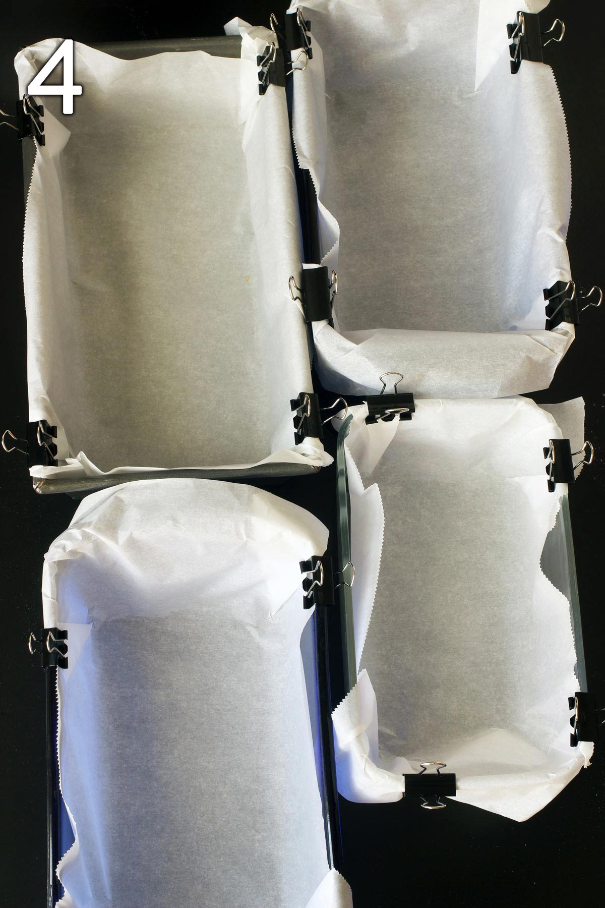 bread loaves lined with parchment paper held with clips.