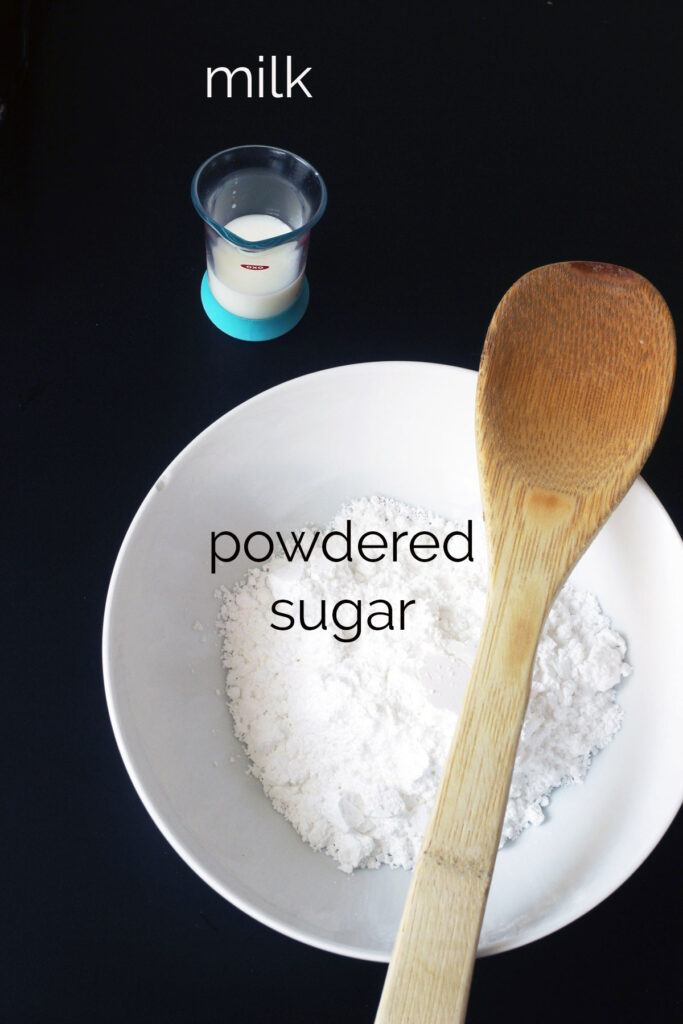 bowl of powdered sugar with measure of milk and wooden spoon.