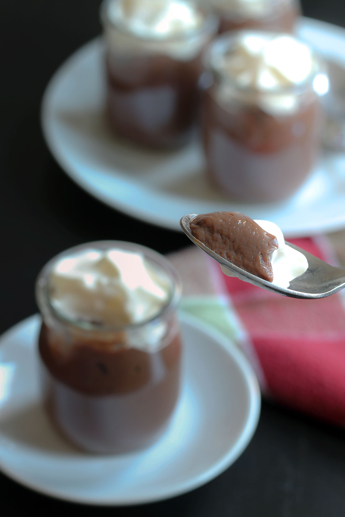 spoonful of pudding in the foreground with pots of chocolate pudding in the background.