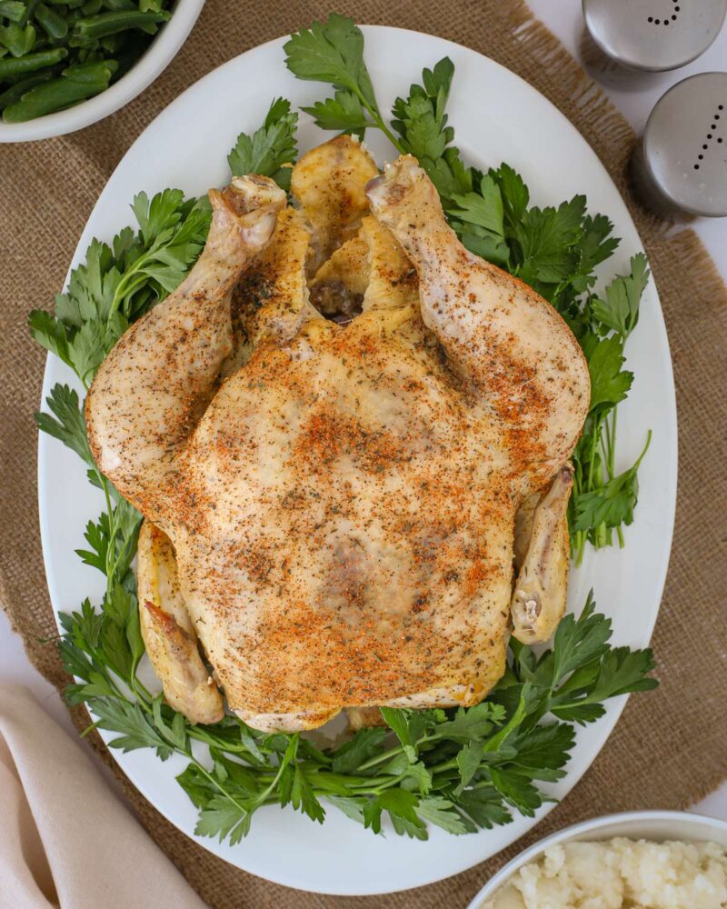 the cooked whole chicken on a platter with fresh parsley.