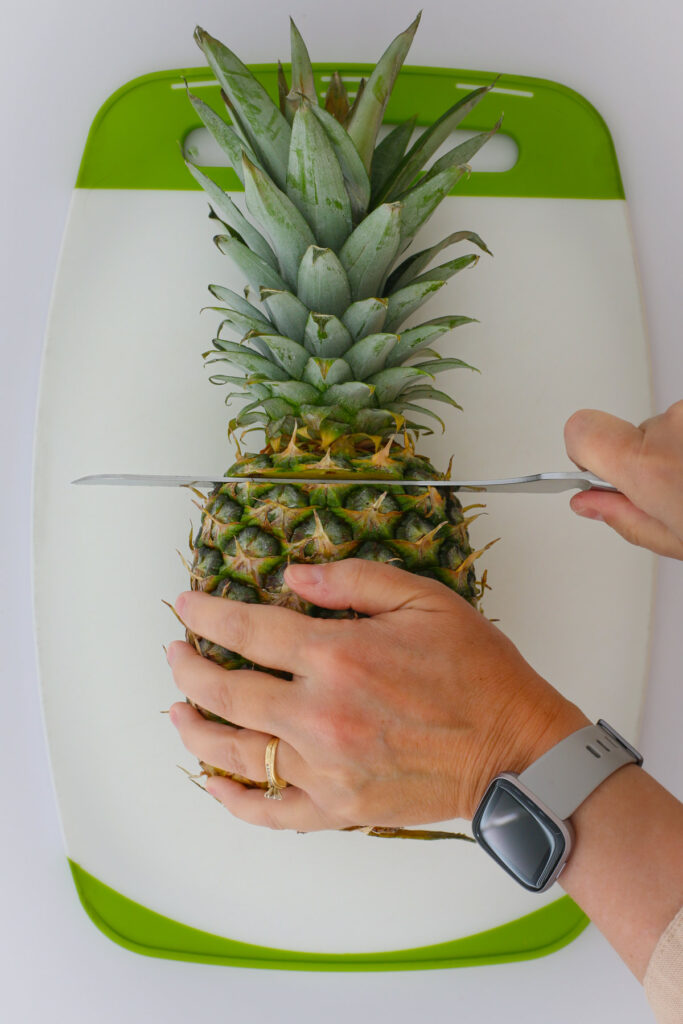 holding the pineapple on its side to cut off the top.