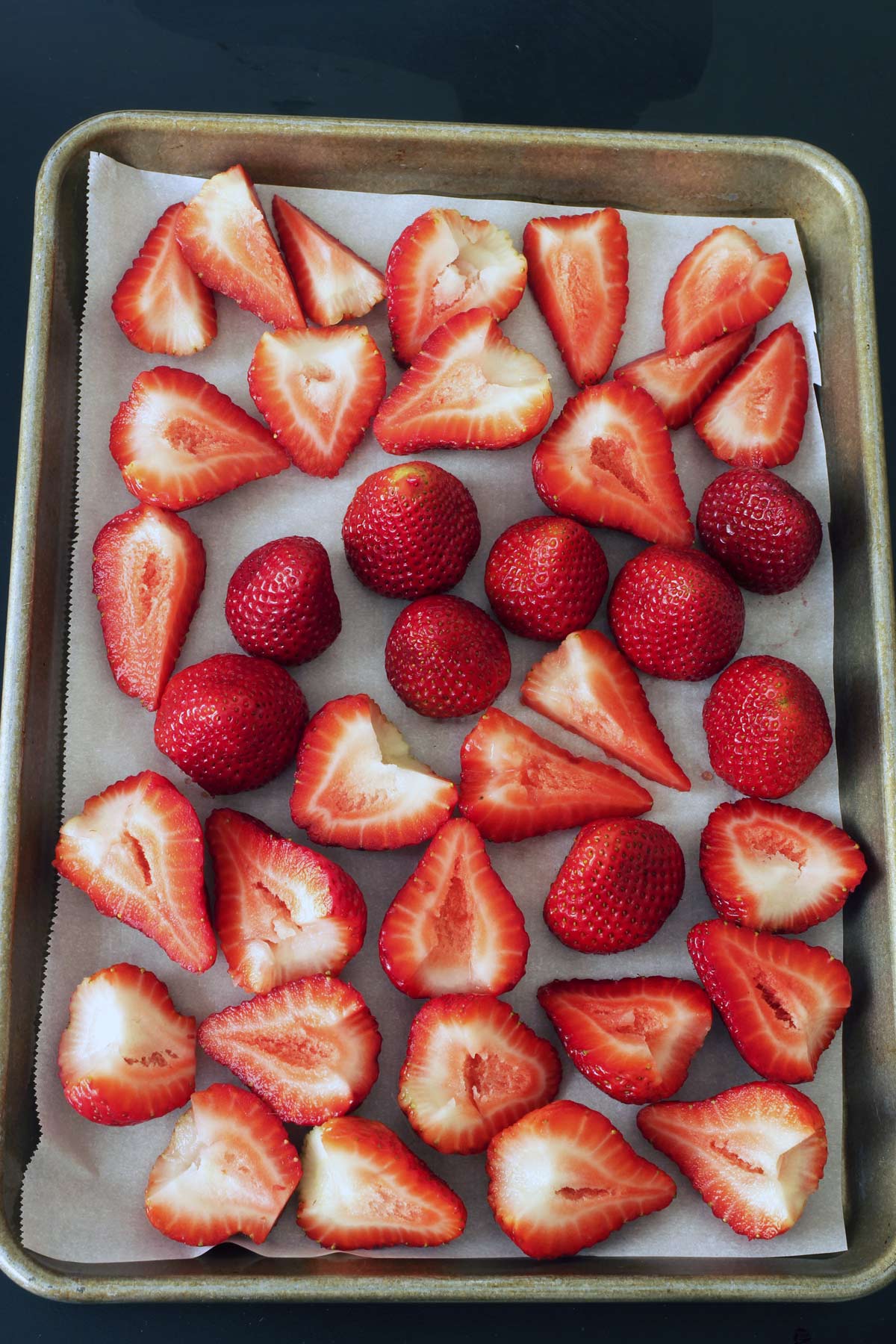 cut and whole strawberries on lined sheet pan.