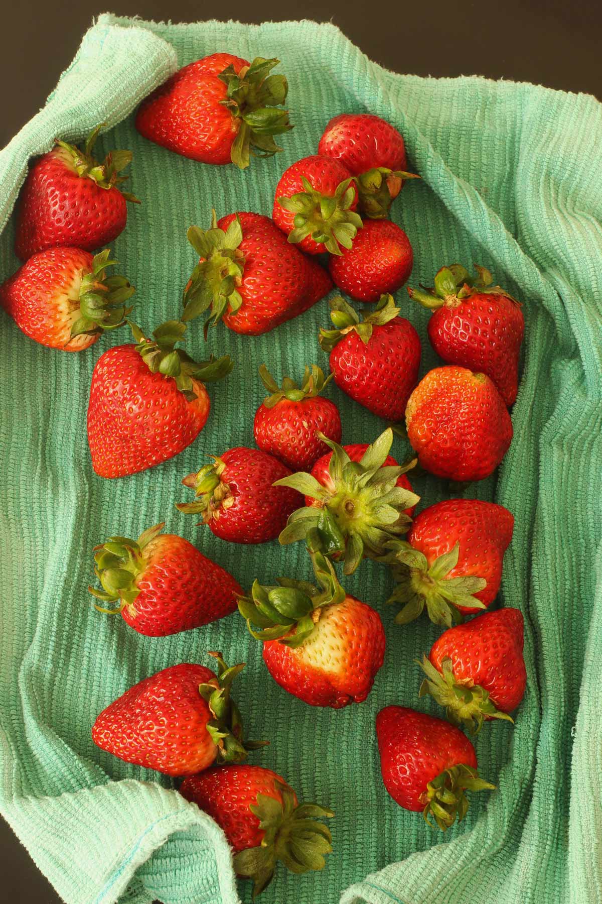 washed strawberries drying on teal kitchen towel.