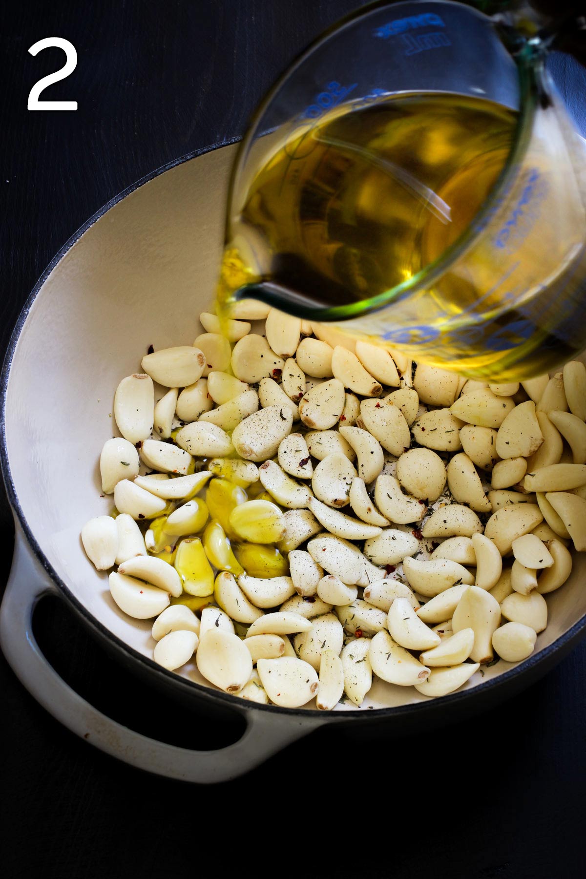 pouring olive oil into dutch oven with garlic cloves and spices.