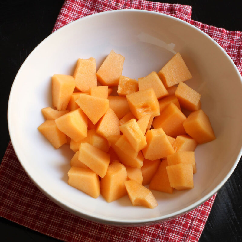 red checked cloth and white bowl of canteloupe cubes.