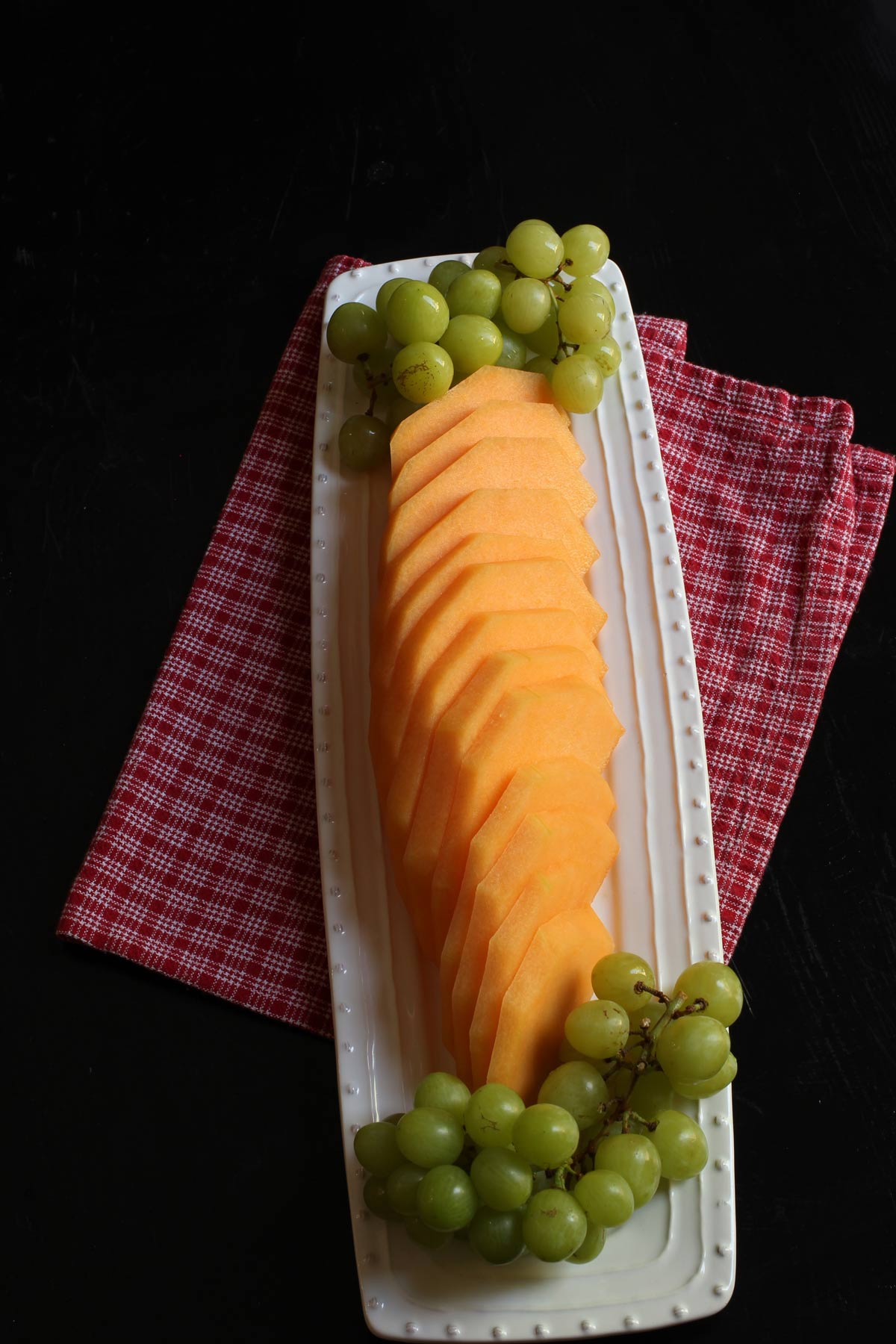 cantaloupe slices on tray with clusters of green grapes.