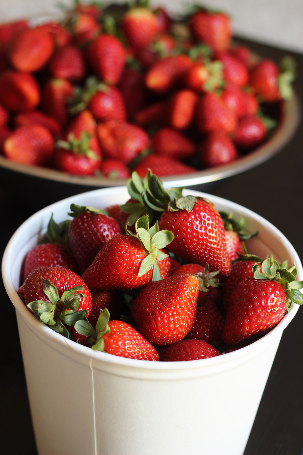 white bucket of strawberries on table next to large bowl of strawberries.