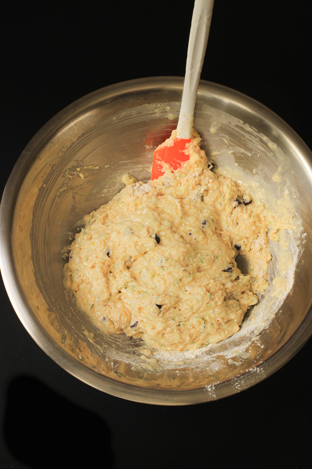 the muffin batter assembled in the metal bowl with a rubber spatula.