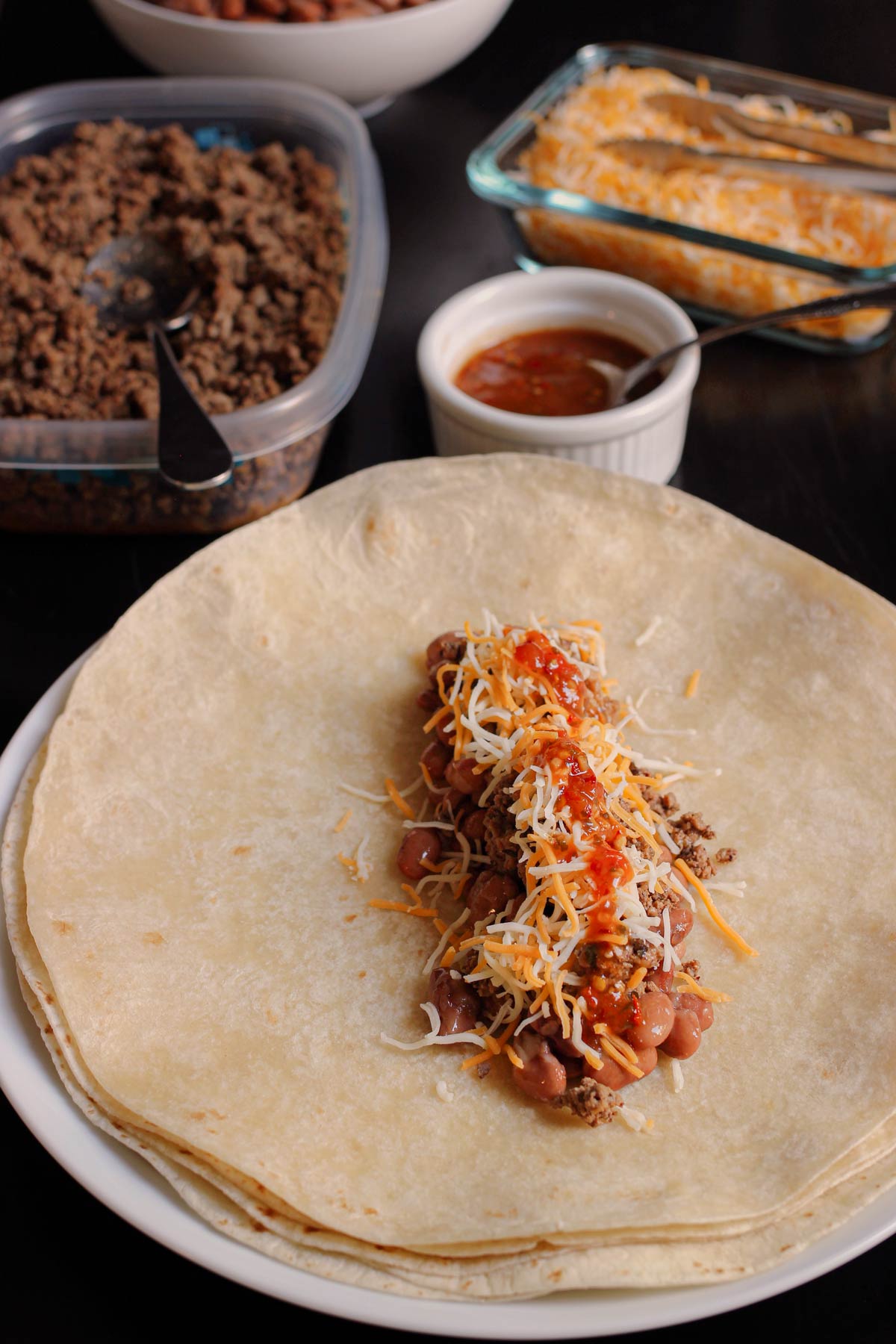 assembling freezer burritos with sauce, cheese, beans, and other fillings.