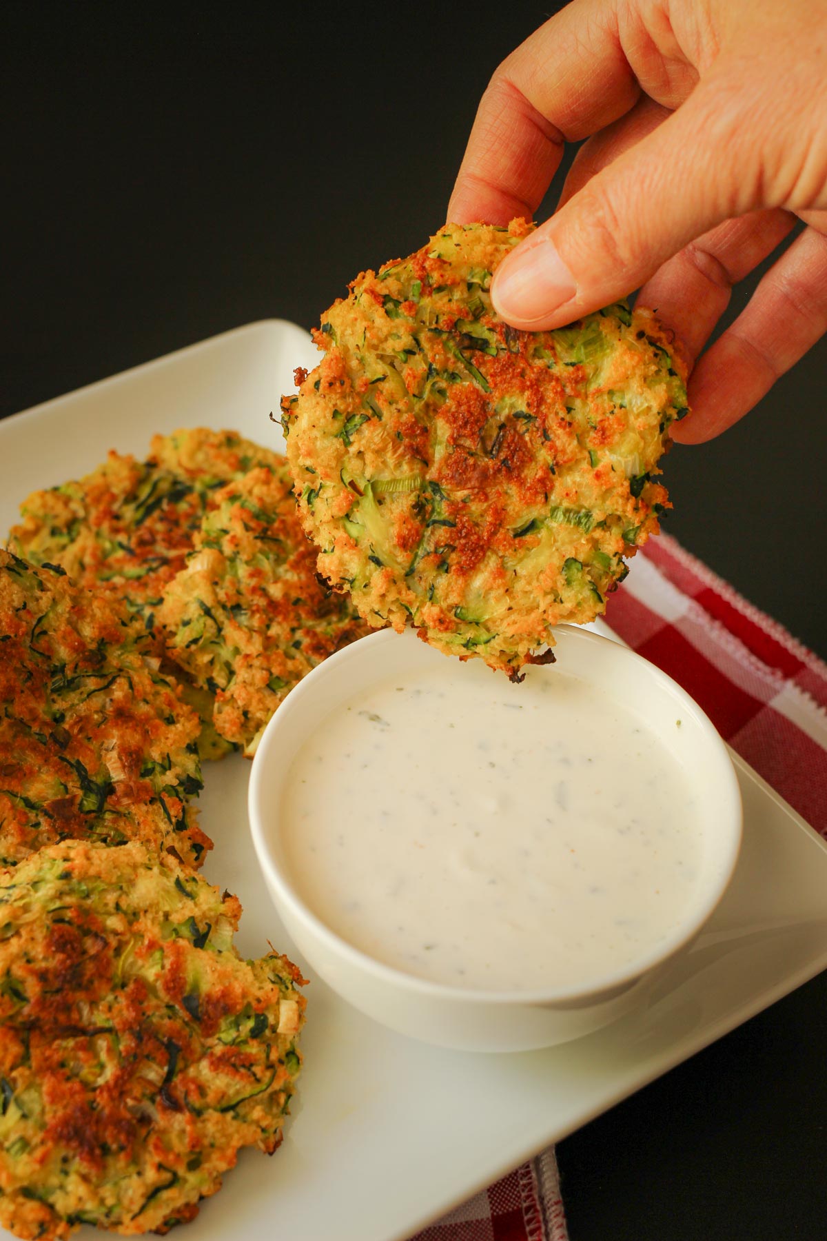 dipping a baked zucchini fritter into a small bowl of ranch dip.