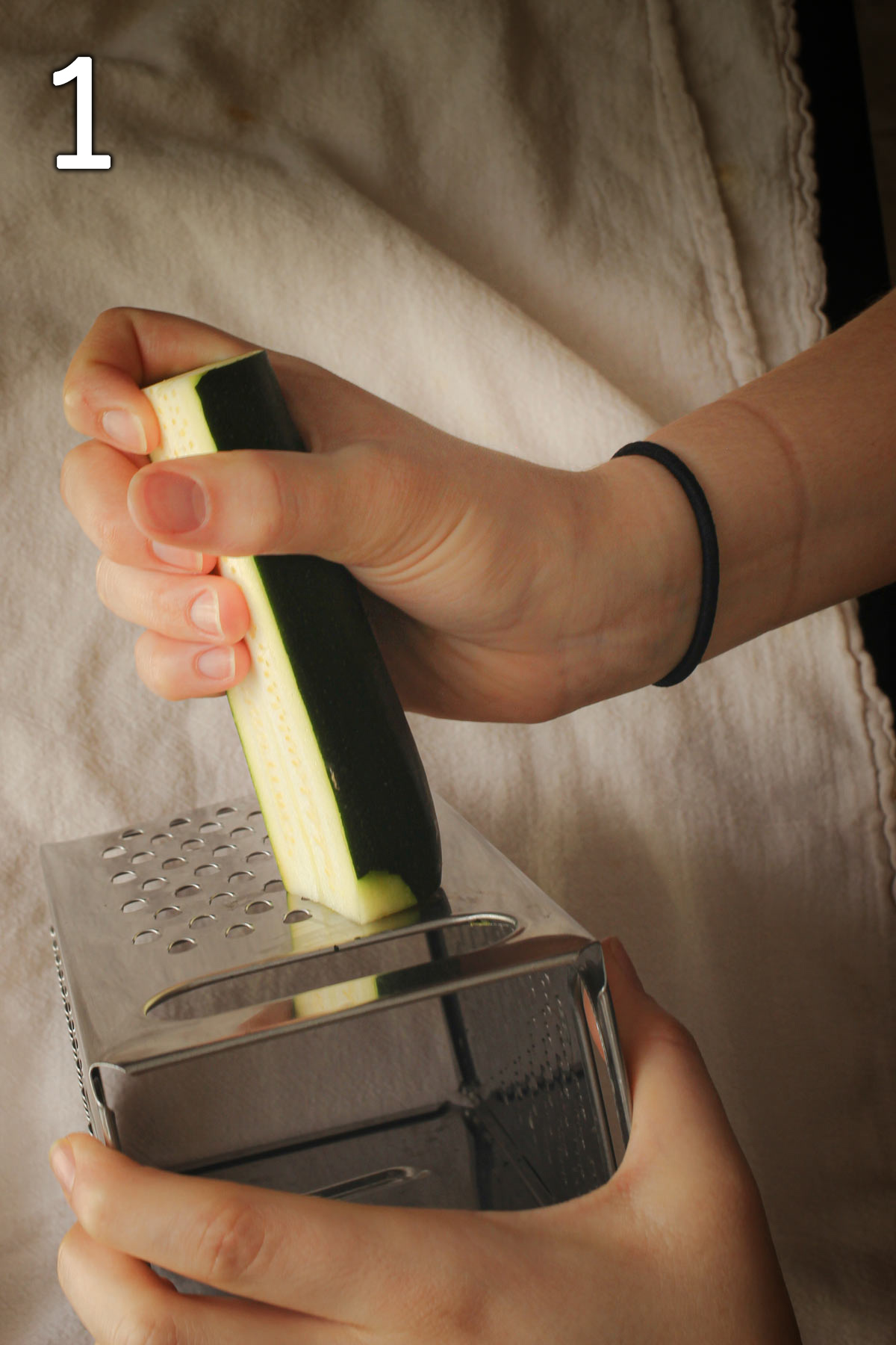 hand holding portion of zucchini alongside box grater to shred it.