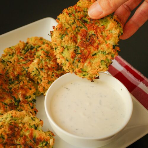 hand dipping a baked zucchini fritter into a small white dish of ranch.