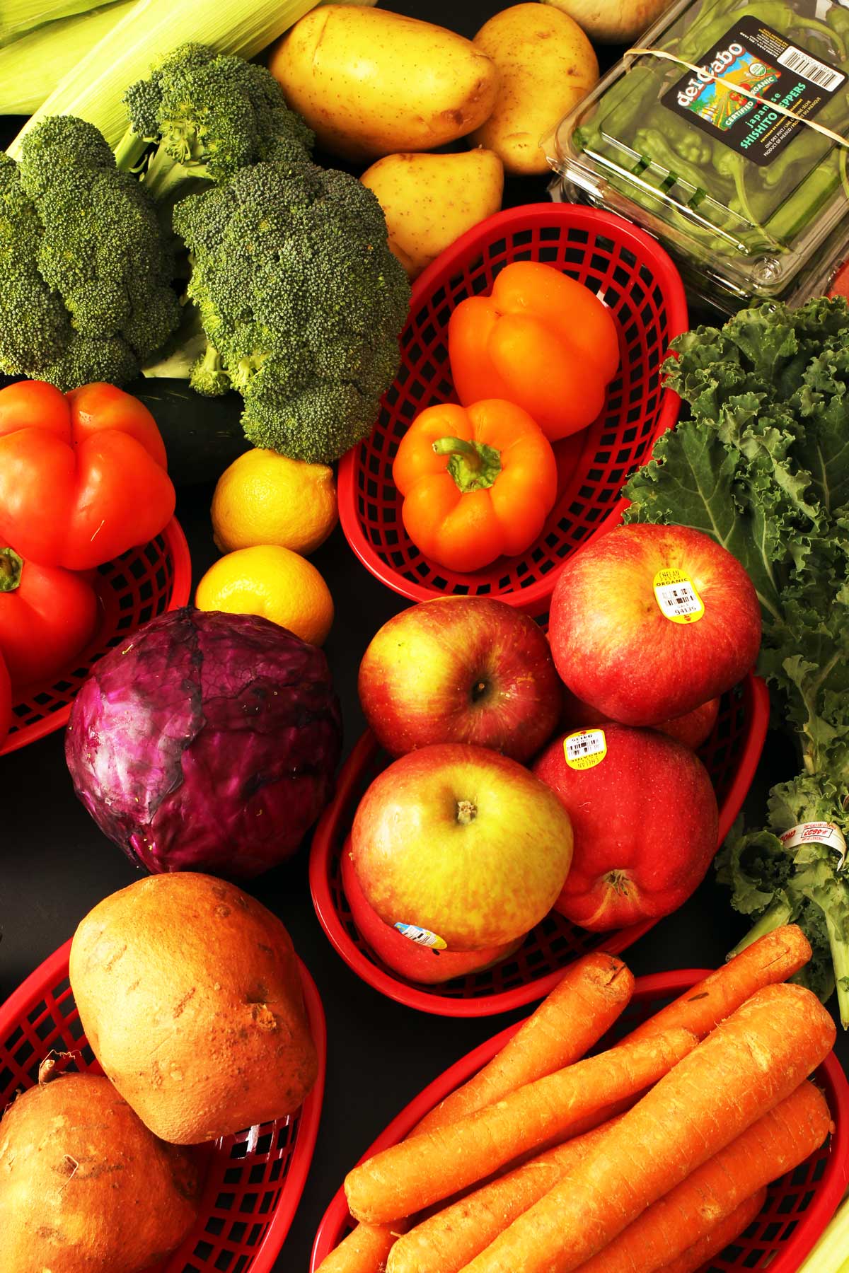 array of fruits and vegetables sorted into red plastic baskets.