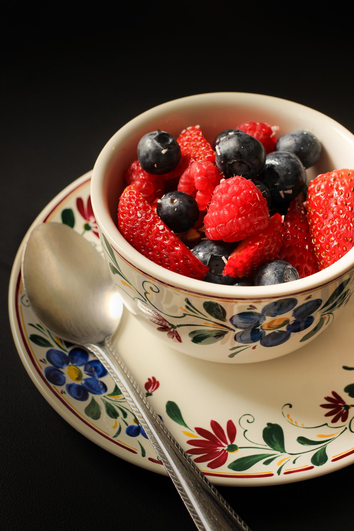 berry salad in a teacup with a spoon on the saucer.