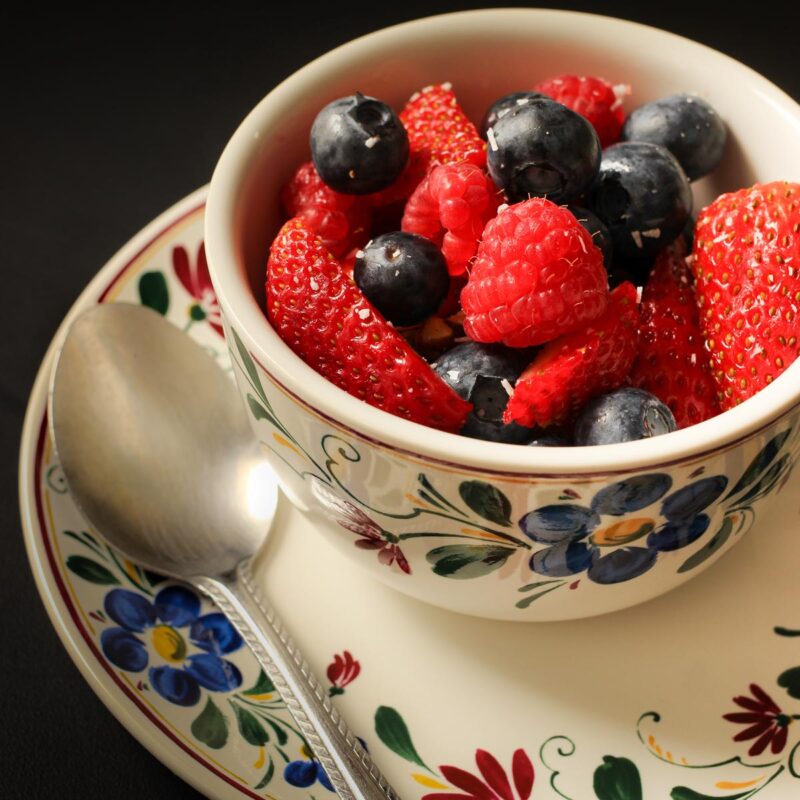 floral teacup loaded high with berry salad with spoon on saucer.