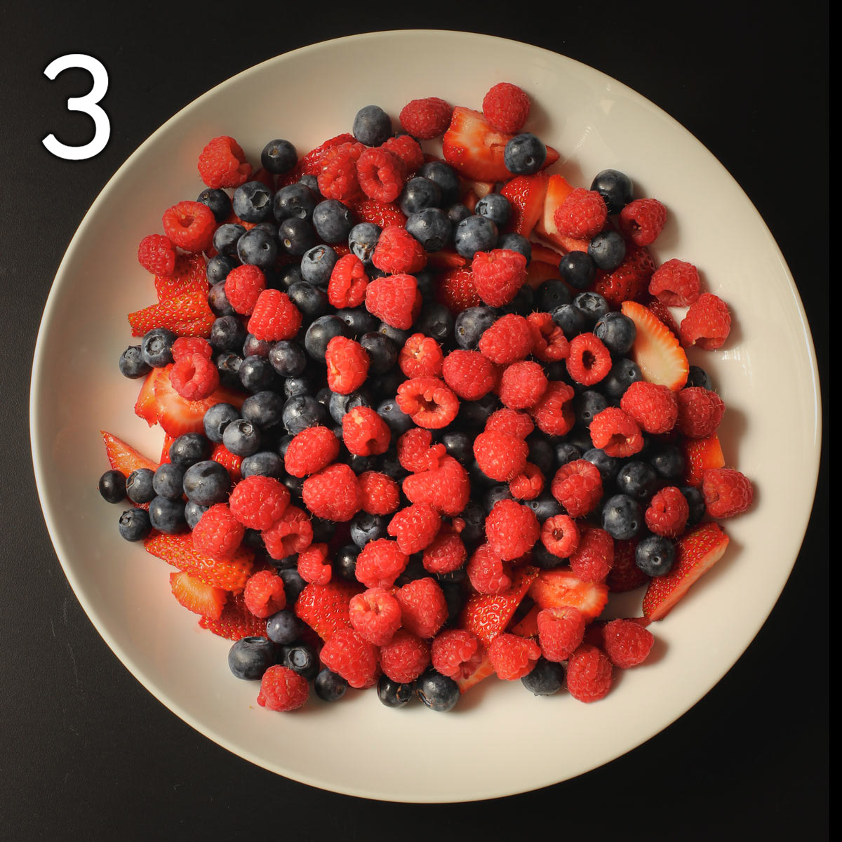 adding raspberries atop blueberries in serving platter.