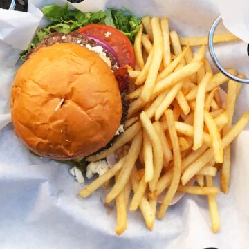 close-up of a deluxe burger in a basket with fries.