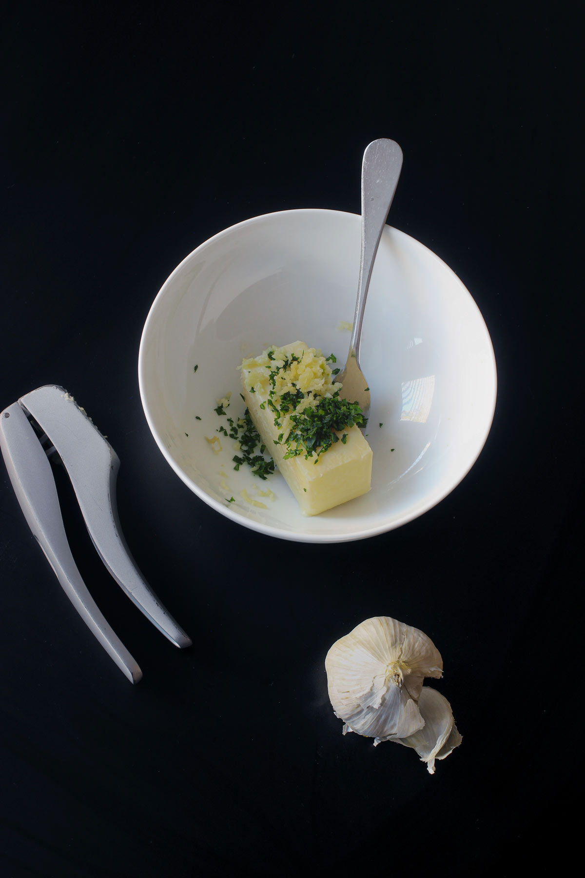 softened stick of butter in a bowl topped with garlic and chopped parsley.