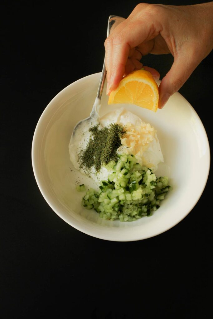 squeezing a wedge of lemon juice into a bowl with all the other garlic yogurt sauce ingredients.