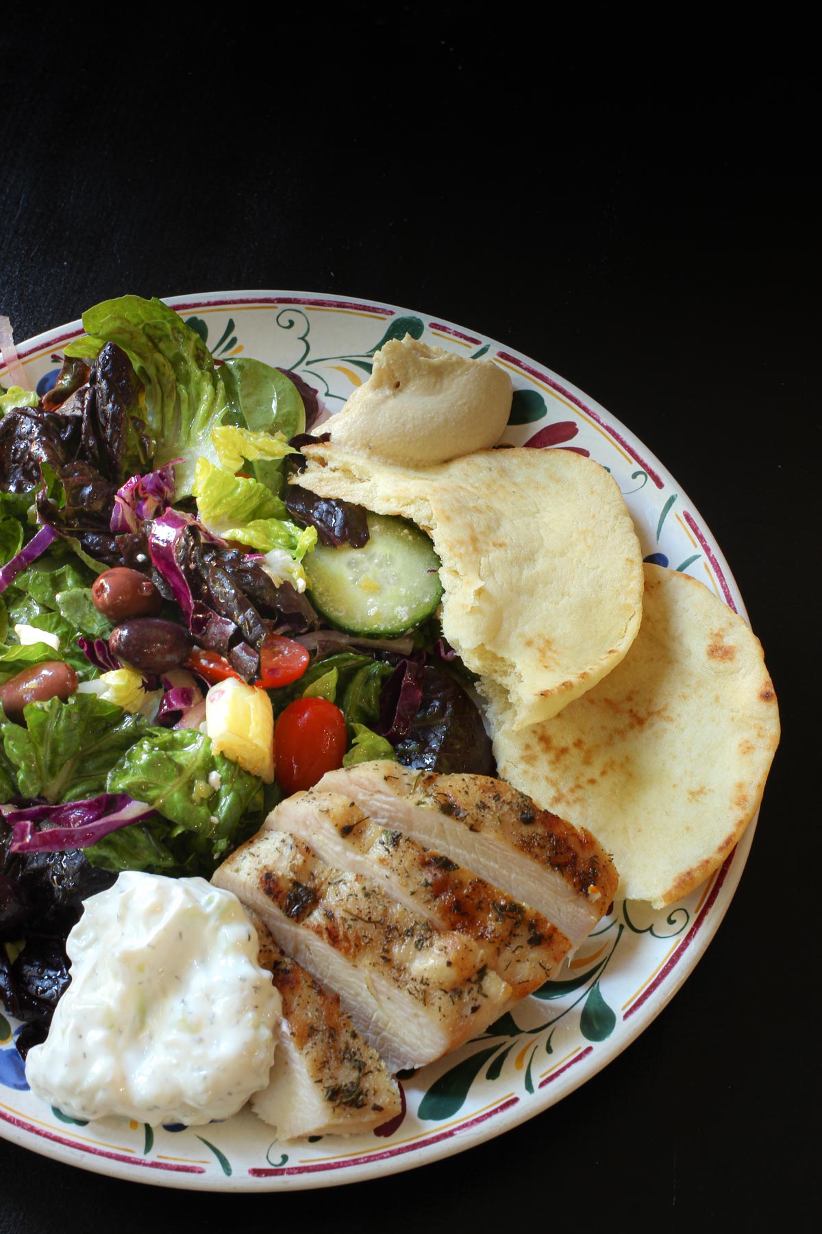 greek meal of grilled chicken with Greek seasoning, pita, salad, and tzatziki.