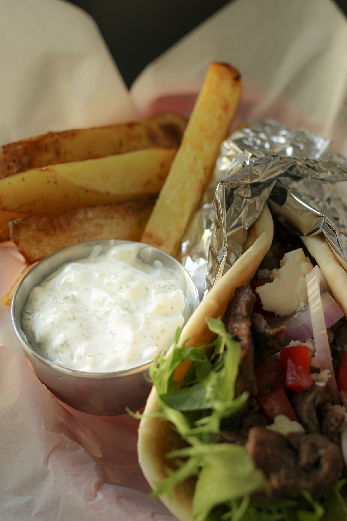 small dish of tzatziki garlic yogurt sauce next to a pita in a basket with fries.