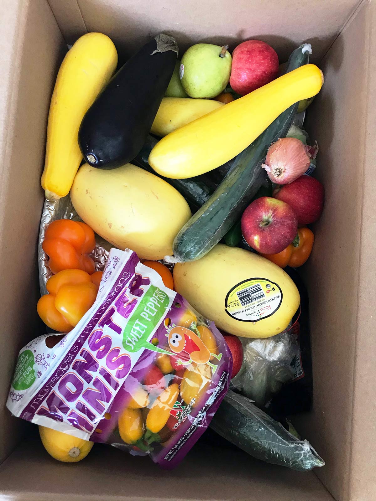 cardboard box full of a mix of fruits and vegetables.