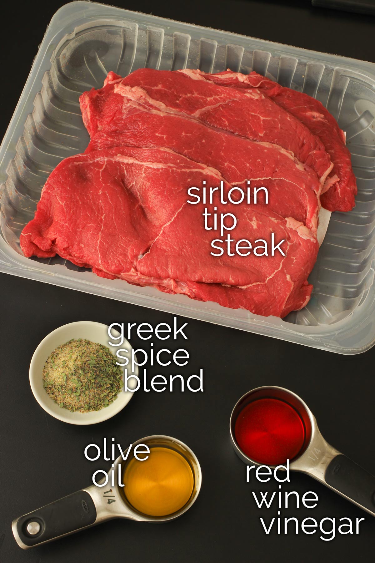 sirloin tip steak in plastic carton on tabletop alongside ingredients for greek marinade.