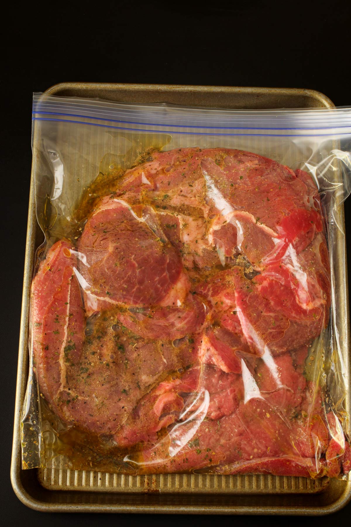bag of steak and greek marinade on tray.