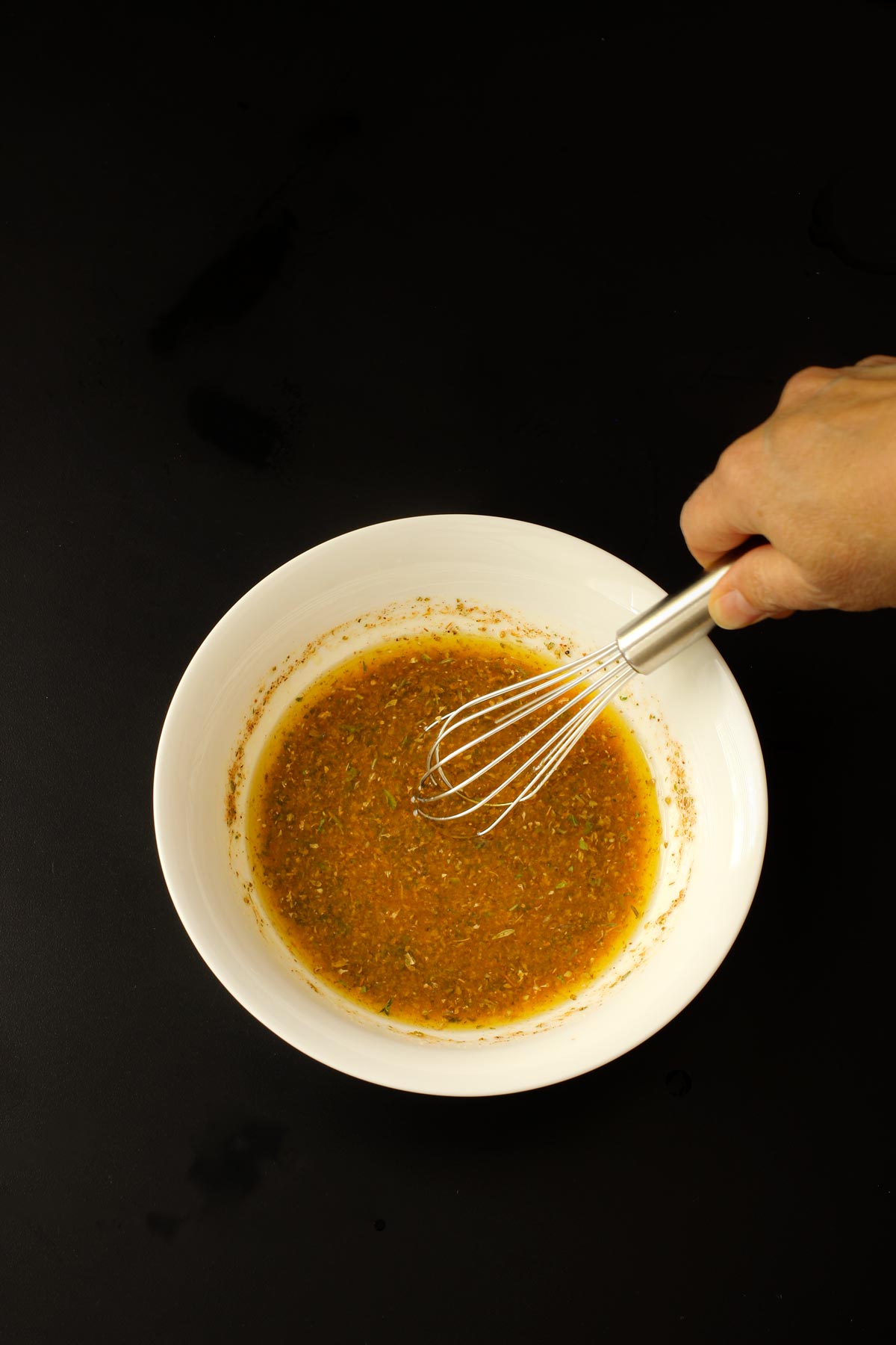 hand whisking greek marinade in a white bowl.