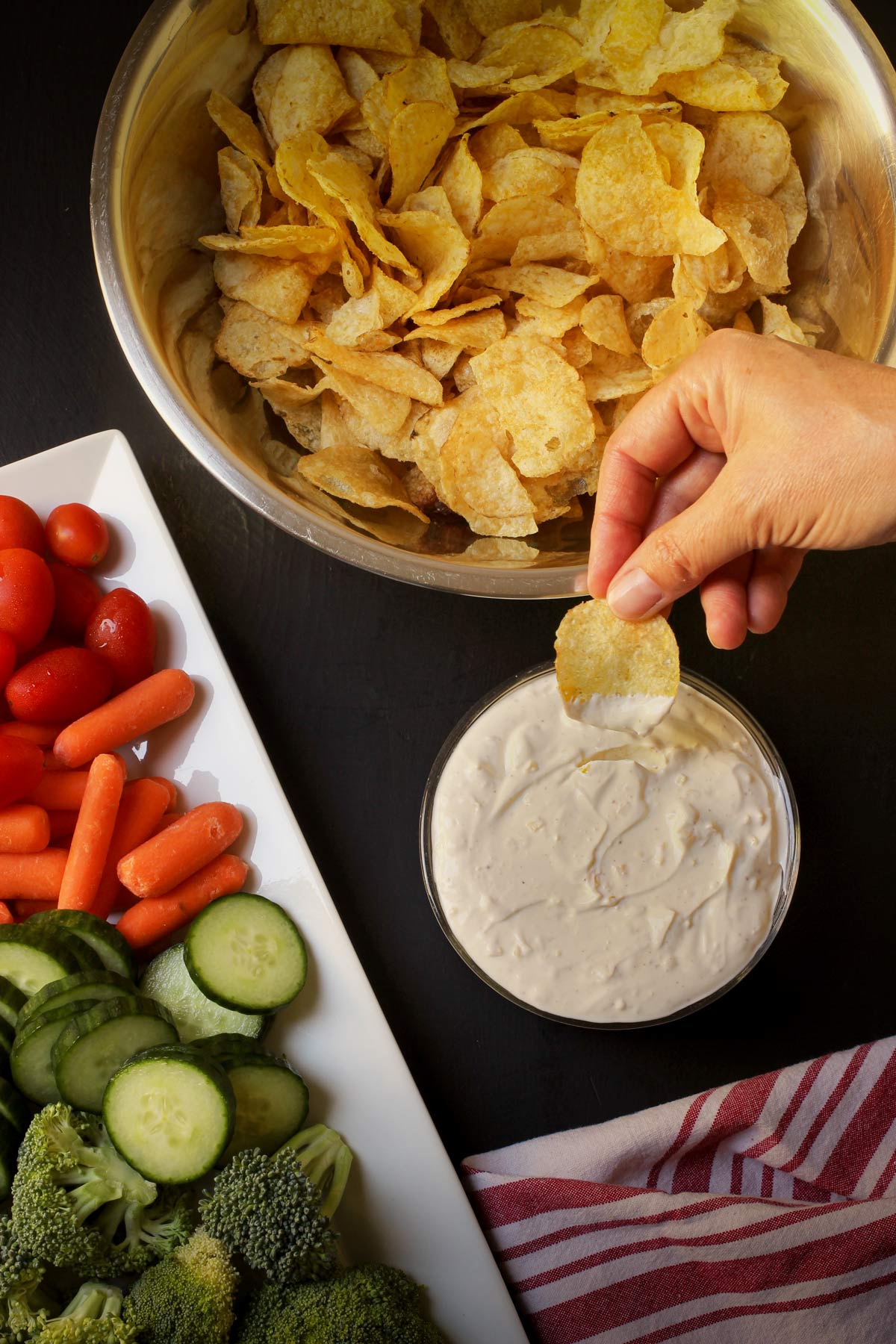 hand dipping potato chip into sour cream and onion dip.