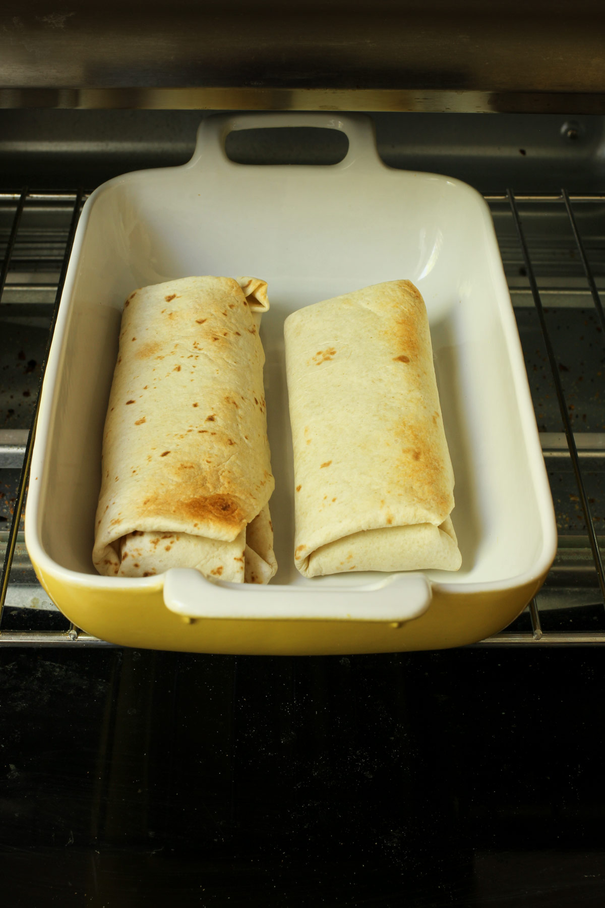 two beef chimichangas baked in a yellow baking dish in the oven.