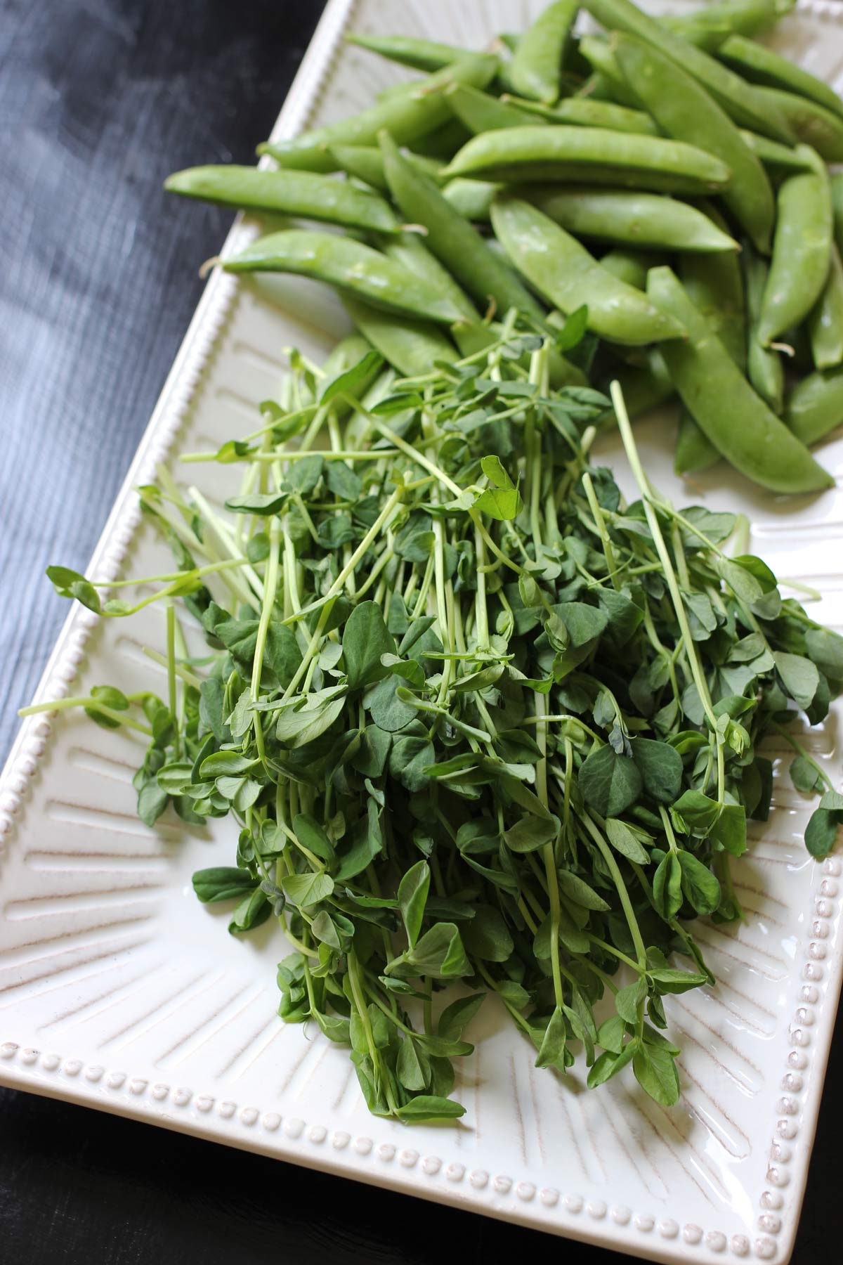 pea tendrils and snap peas piled on a platter.