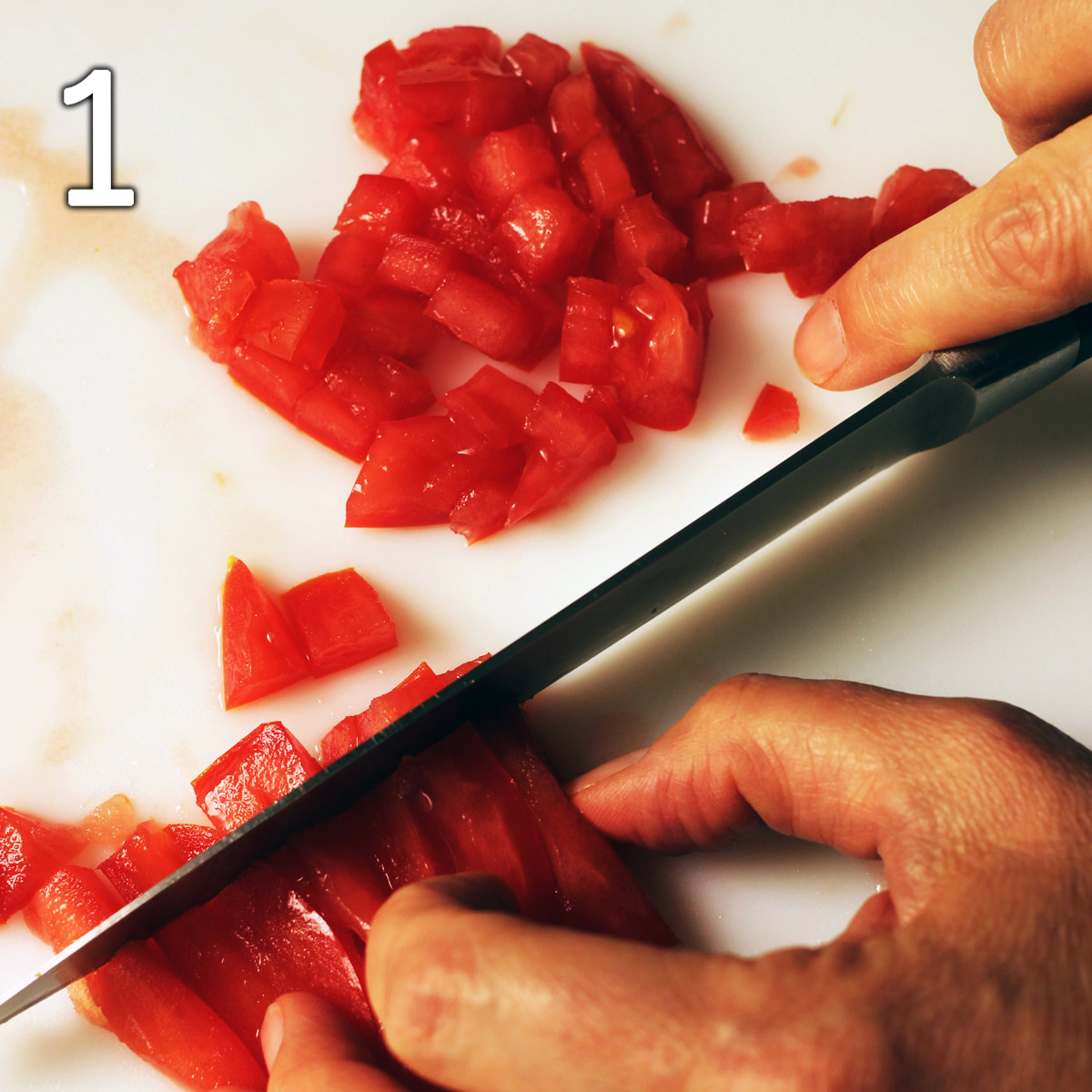 chopping tomatoes on a white cutting board.