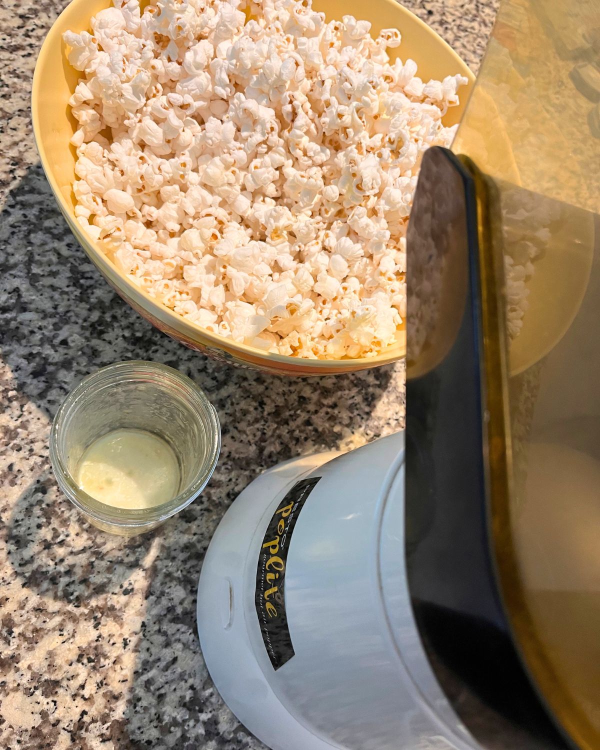 air popped corn in a yellow bowl near an air popper and a jar of melted butter.