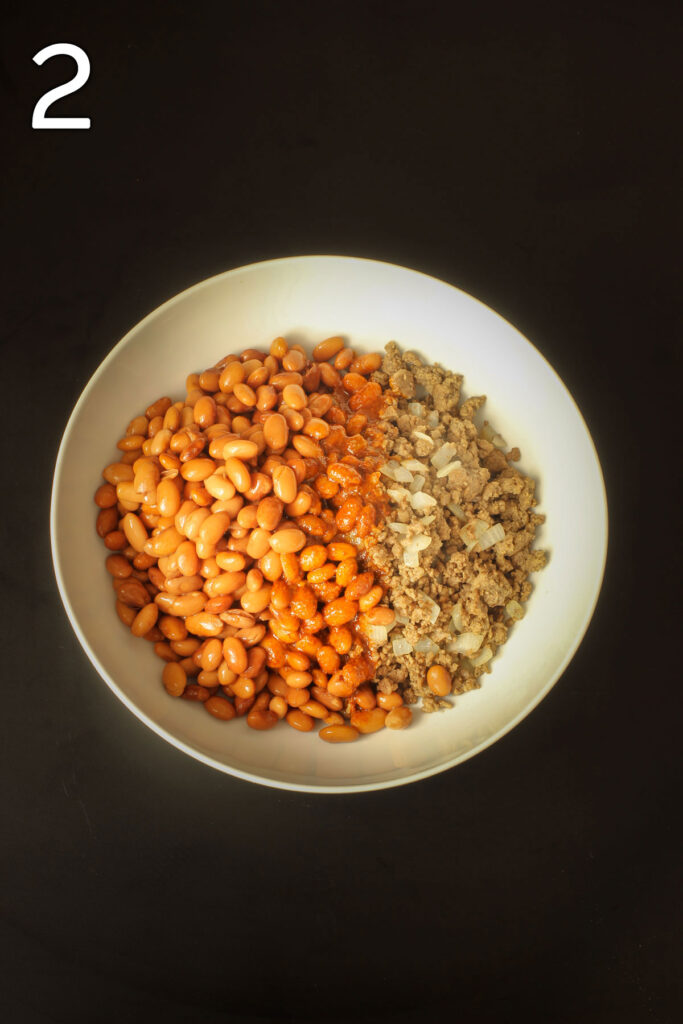 beans and beef with red sauce in white bowl.