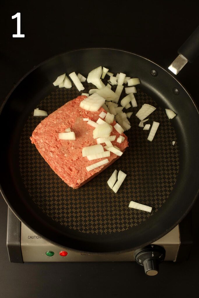 brick of ground beef in skillet with chopped onion.