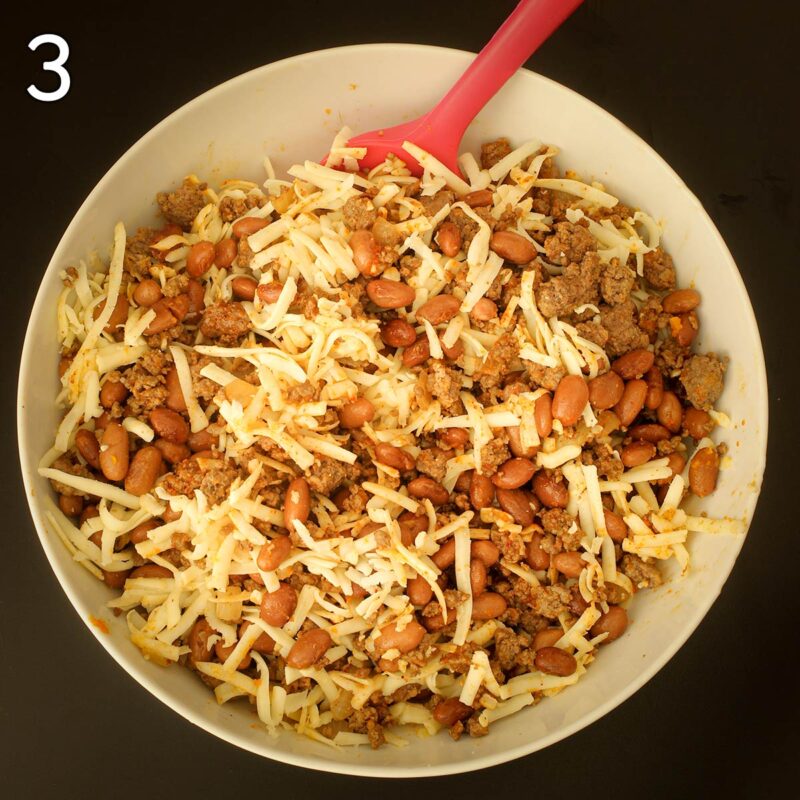 mixing in shredded jack cheese into the bean and beef mixture in white bowl.