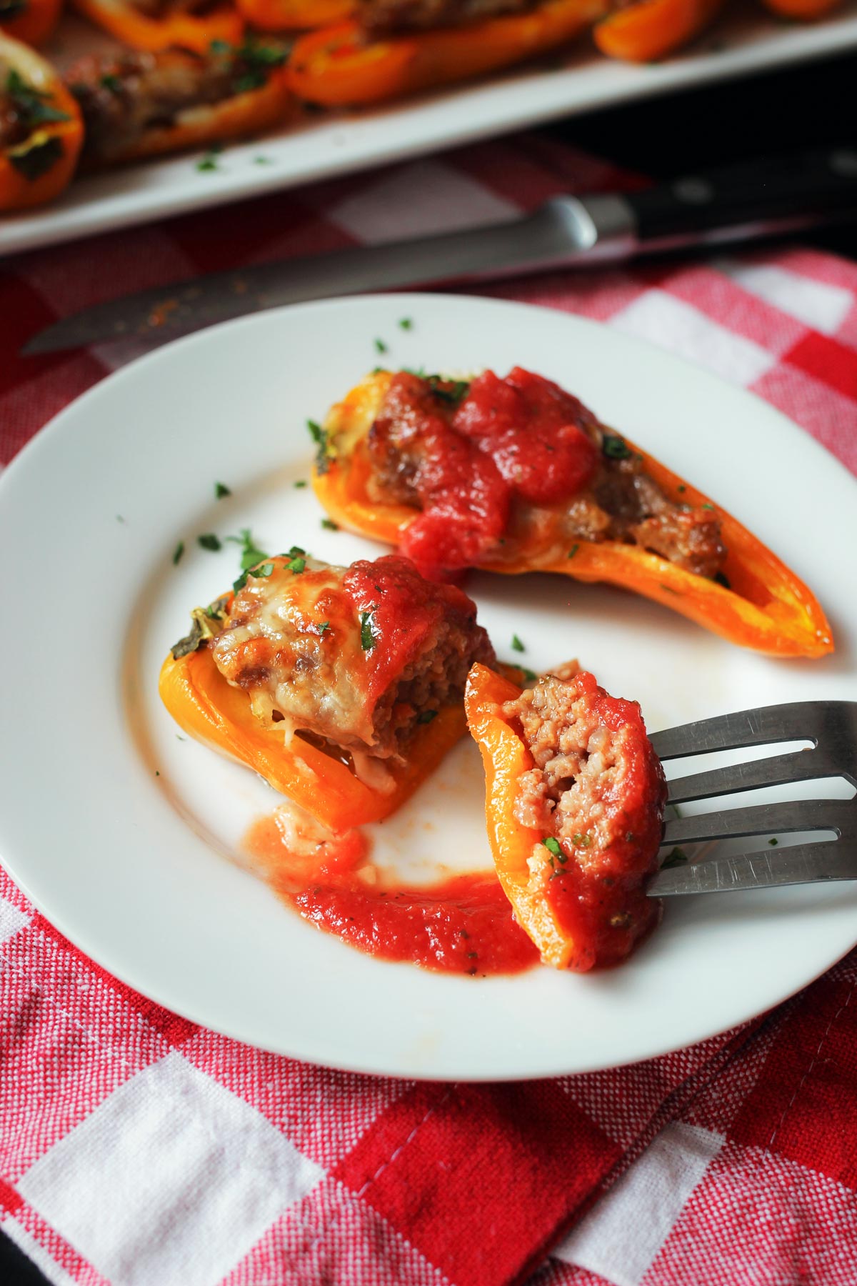 two stuffed mini peppers on a small appetizer plate, one cut in half with a bite on the fork.
