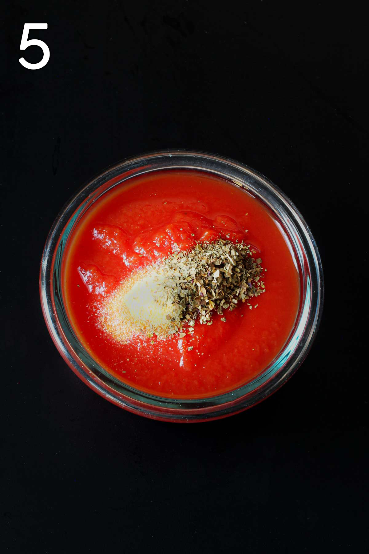 tomato sauce and herbs in small glass bowl on black tabletop.