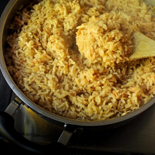 wooden spoon scooping up rice from a pan of seasoned rice pilaf.