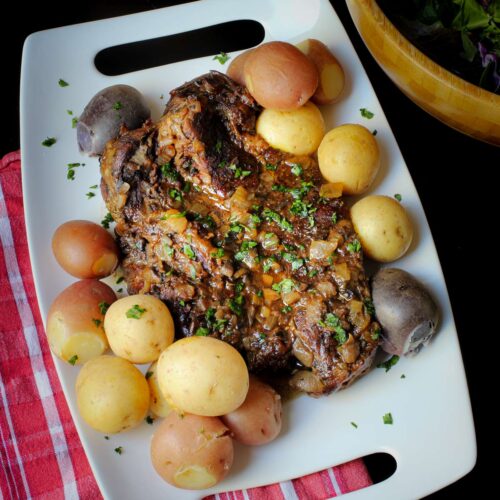 slow cooked chuck roast on platter with herbs and tri-color potatoes.