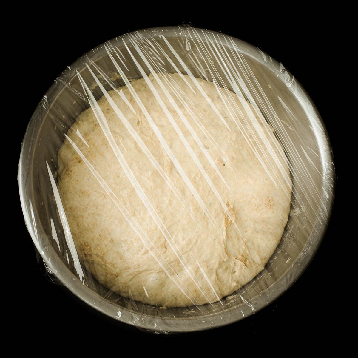 dough ball risen in metal bowl covered with plastic wrap.
