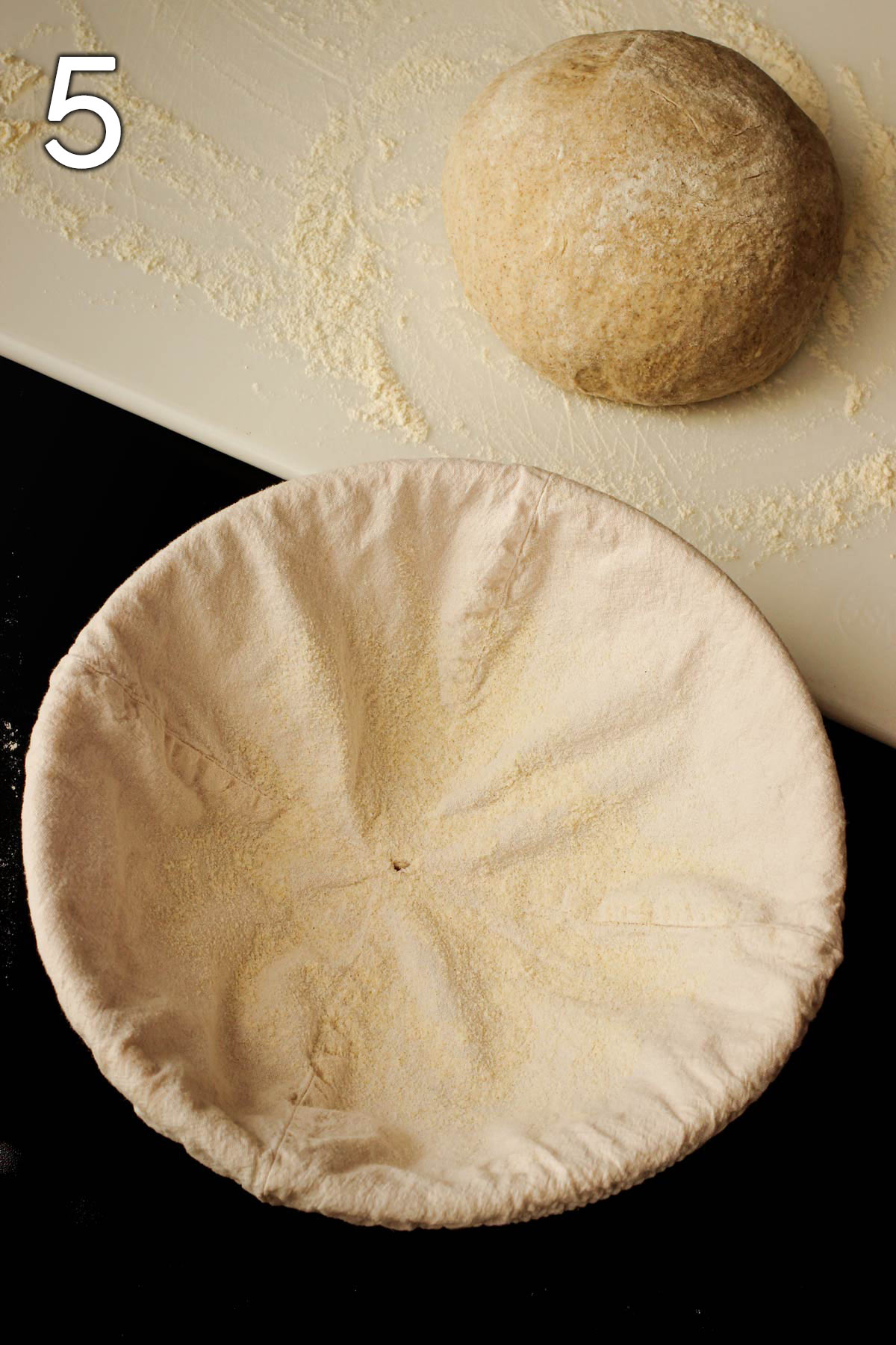 cloth covered banneton dusted with rice flour next to dough ball on floured work surface.