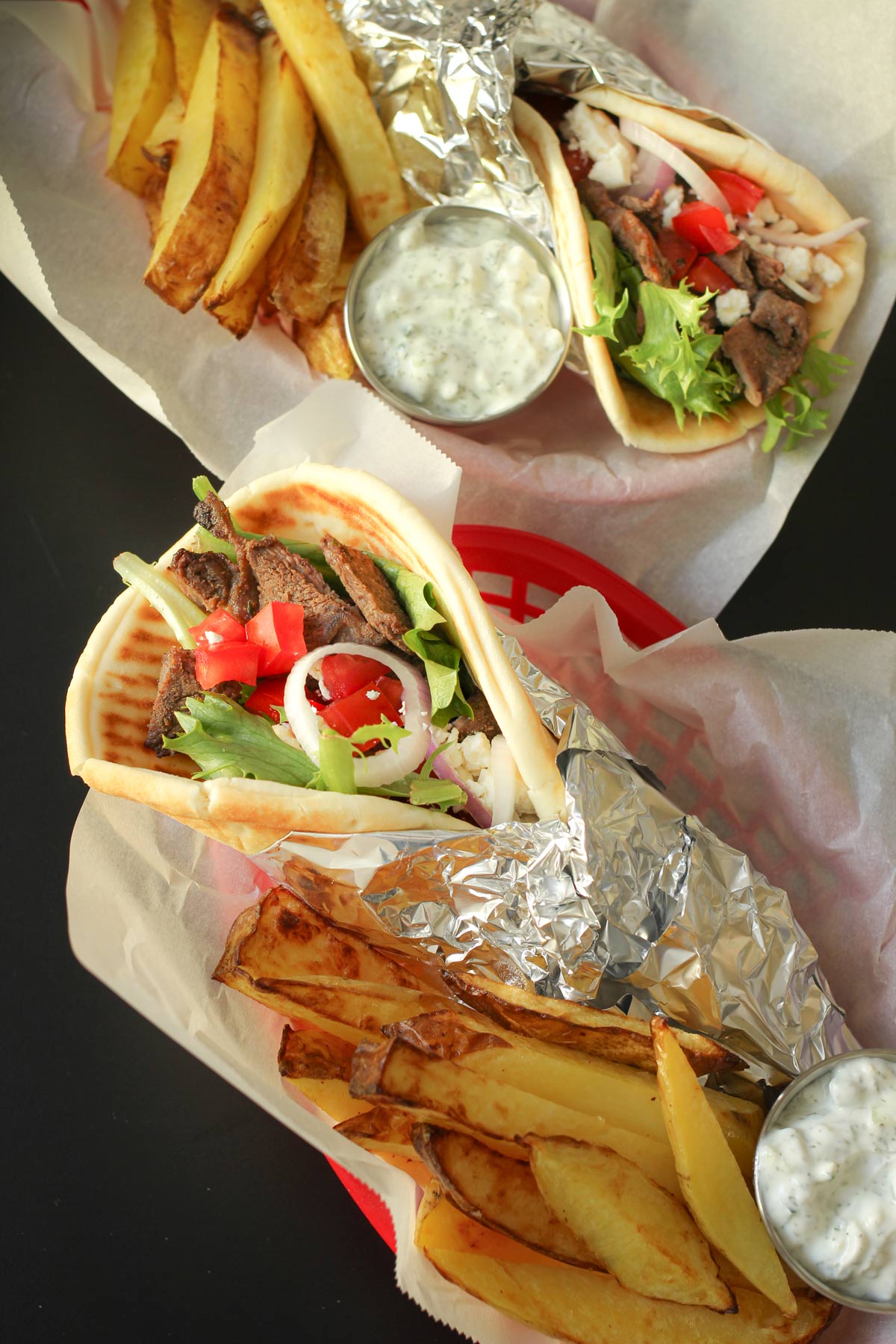 steak pitas in baskets with fries and cups of garlic yogurt sauce.