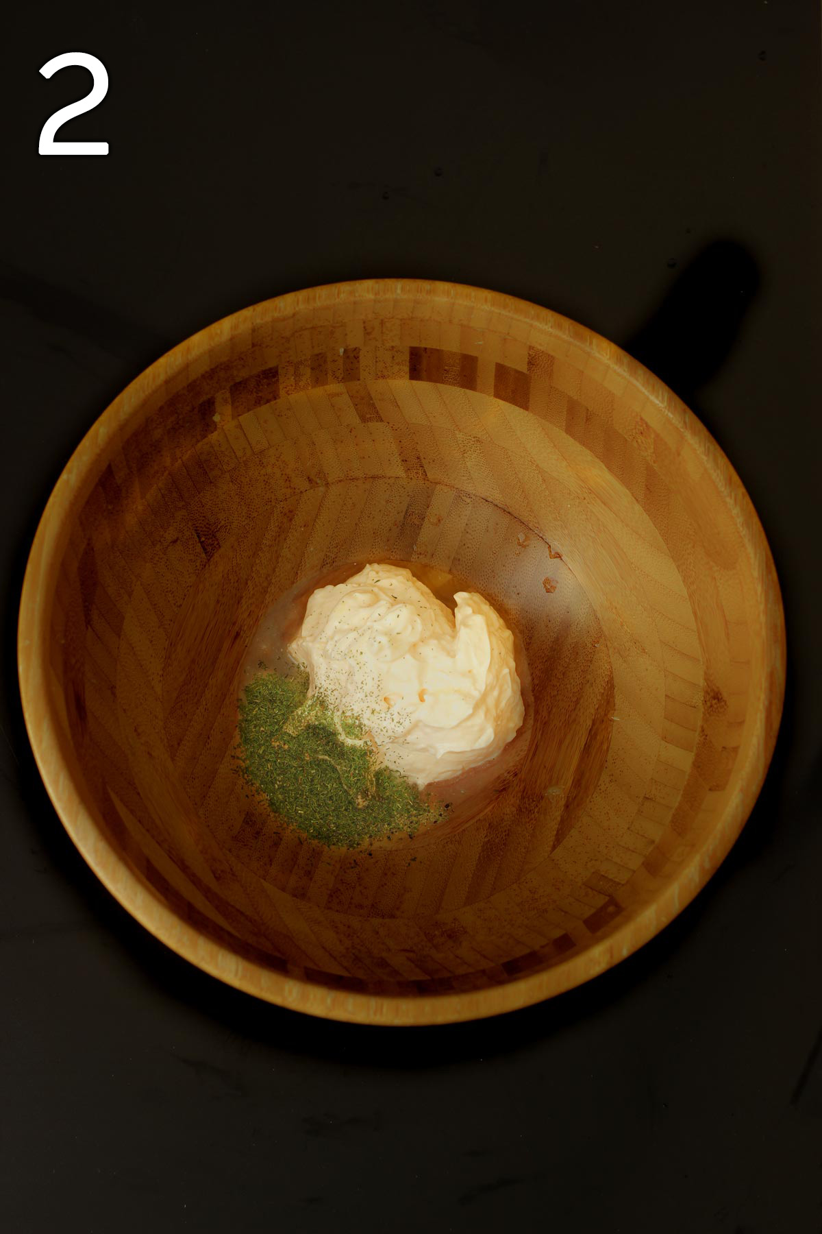 dressing ingredients in the bottom of a large wooden salad bowl.