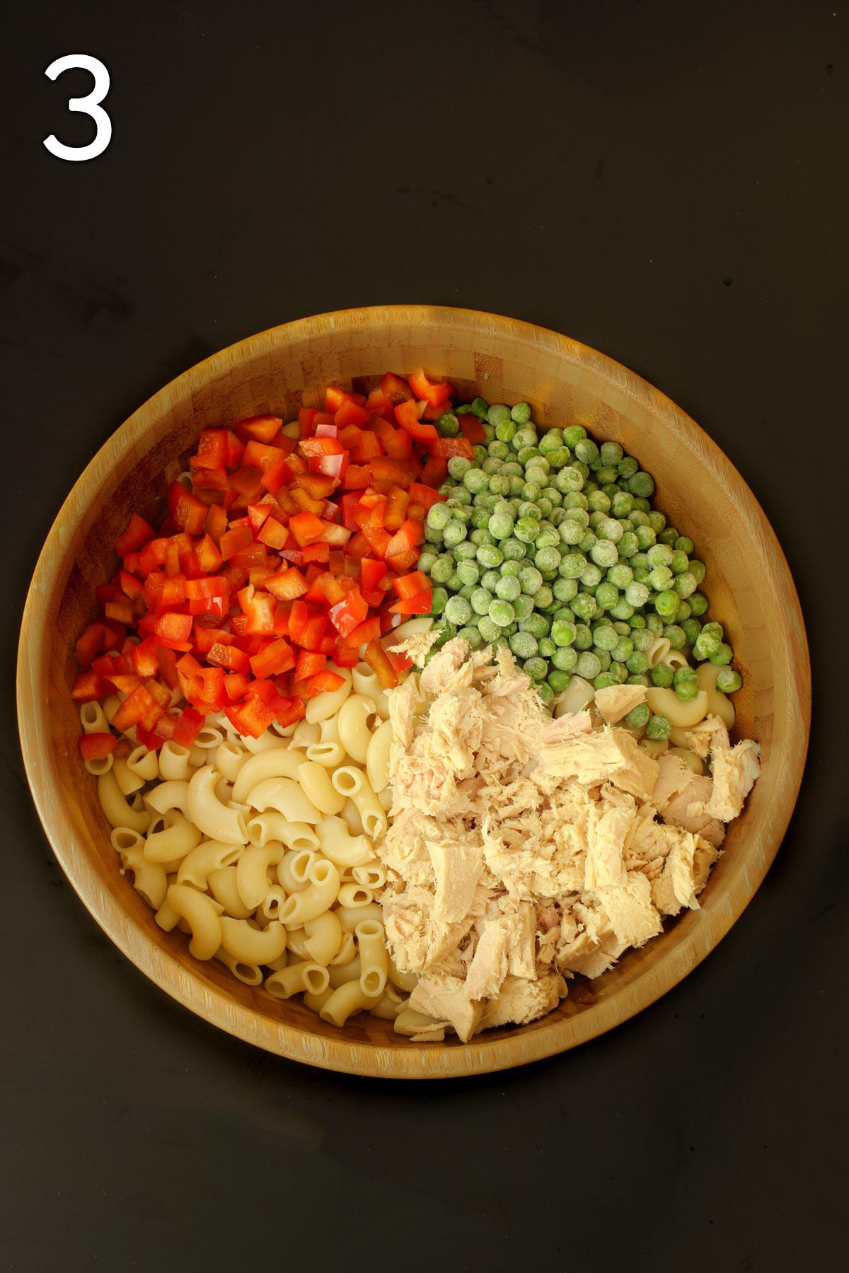 peppers, peas, tuna, and pasta arranged in quarters in the wooden bowl.